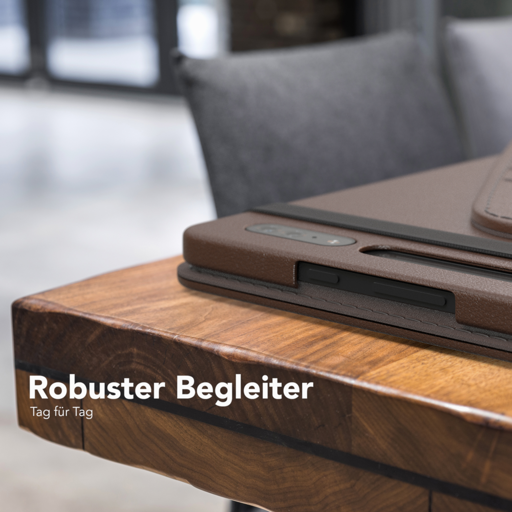 Braune Handyhülle auf einem Holztisch, grauer Stuhl im Hintergrund. Das Wort 'Robust'.