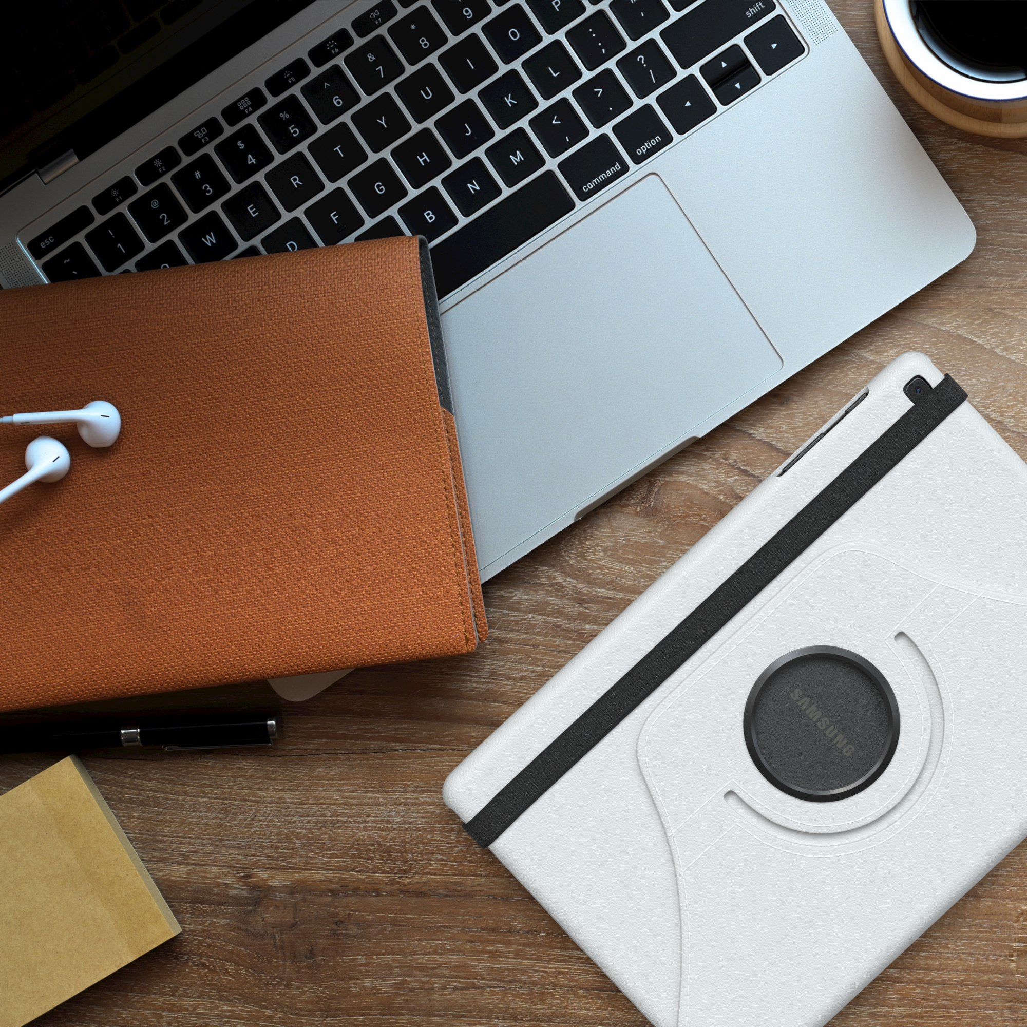 Draufsicht auf Laptop, Tablet und Zubehör auf einem Holztisch. Weiße Tablet-Hülle mit schwarzem Band.