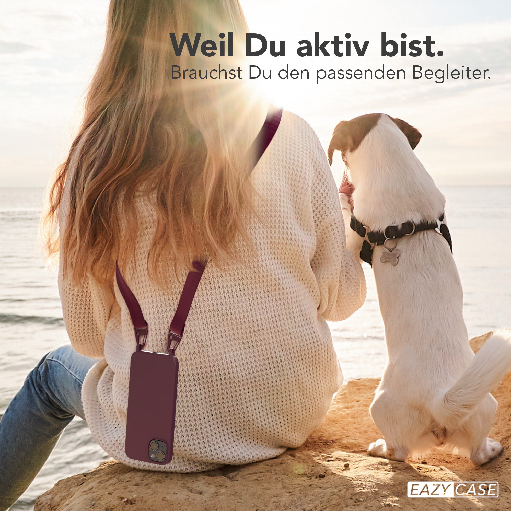 Frau und Hund am Strand. Frau hat Handyhülle an einem Riemen.
