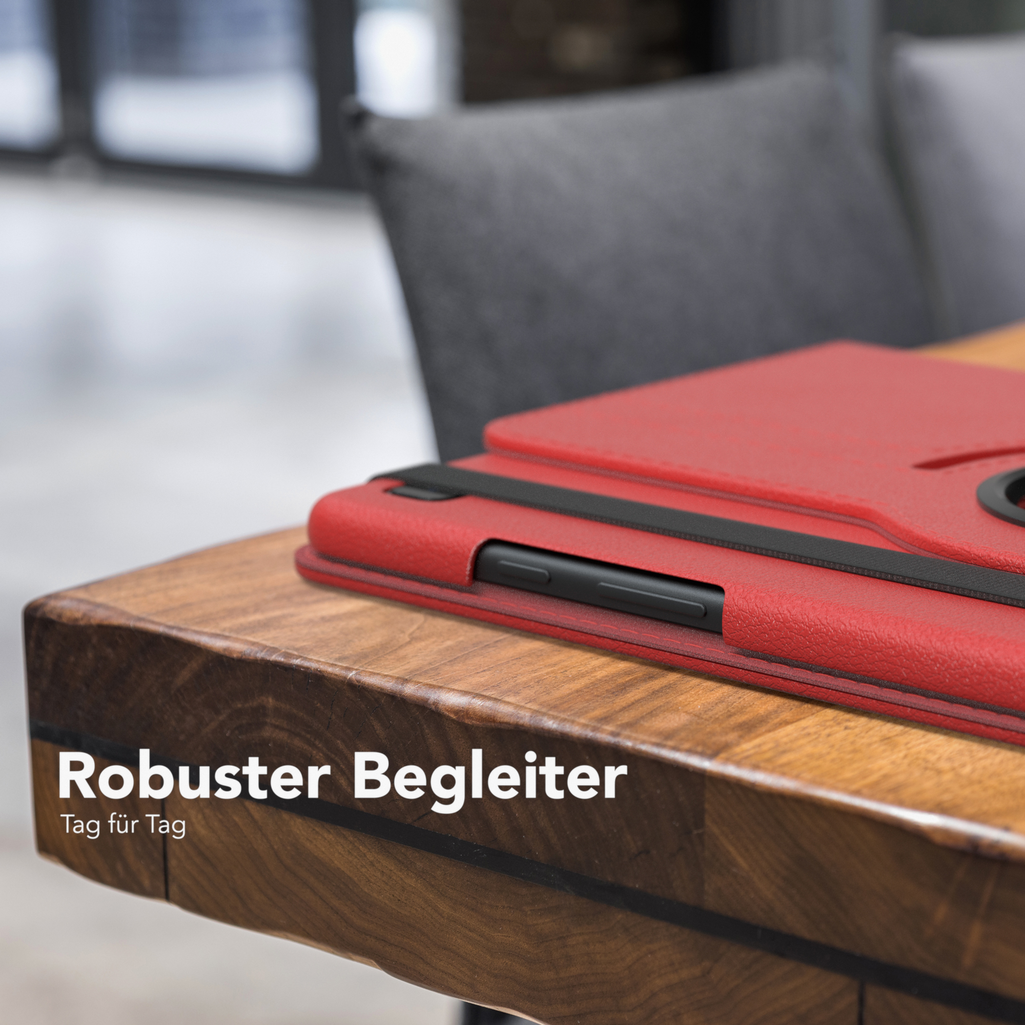 Rote Tablethülle auf einem Holztisch mit schwarzem Riemen und Stuhl im Hintergrund.
