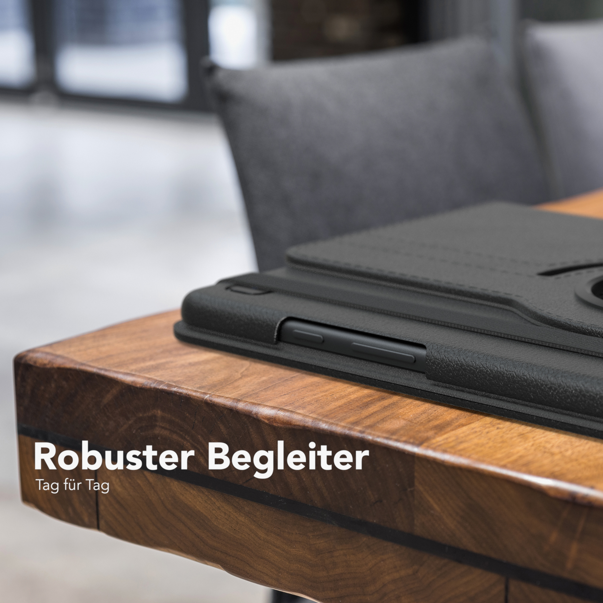 Eine schwarze Tablet-Hülle auf einem Holztisch, mit einem Stuhl im Hintergrund.