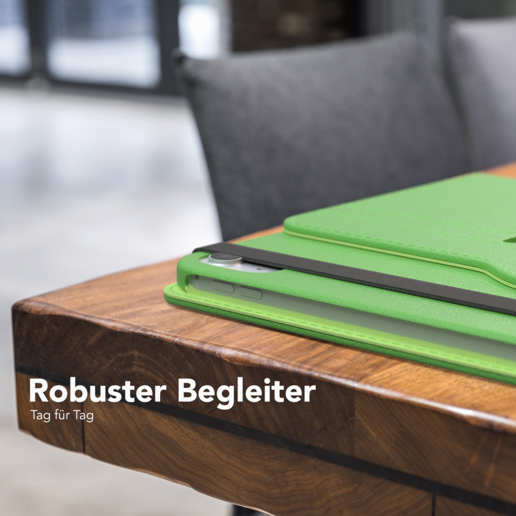 Grüne Tablet-Hülle auf Holztisch. Grauer Stuhl im Hintergrund.