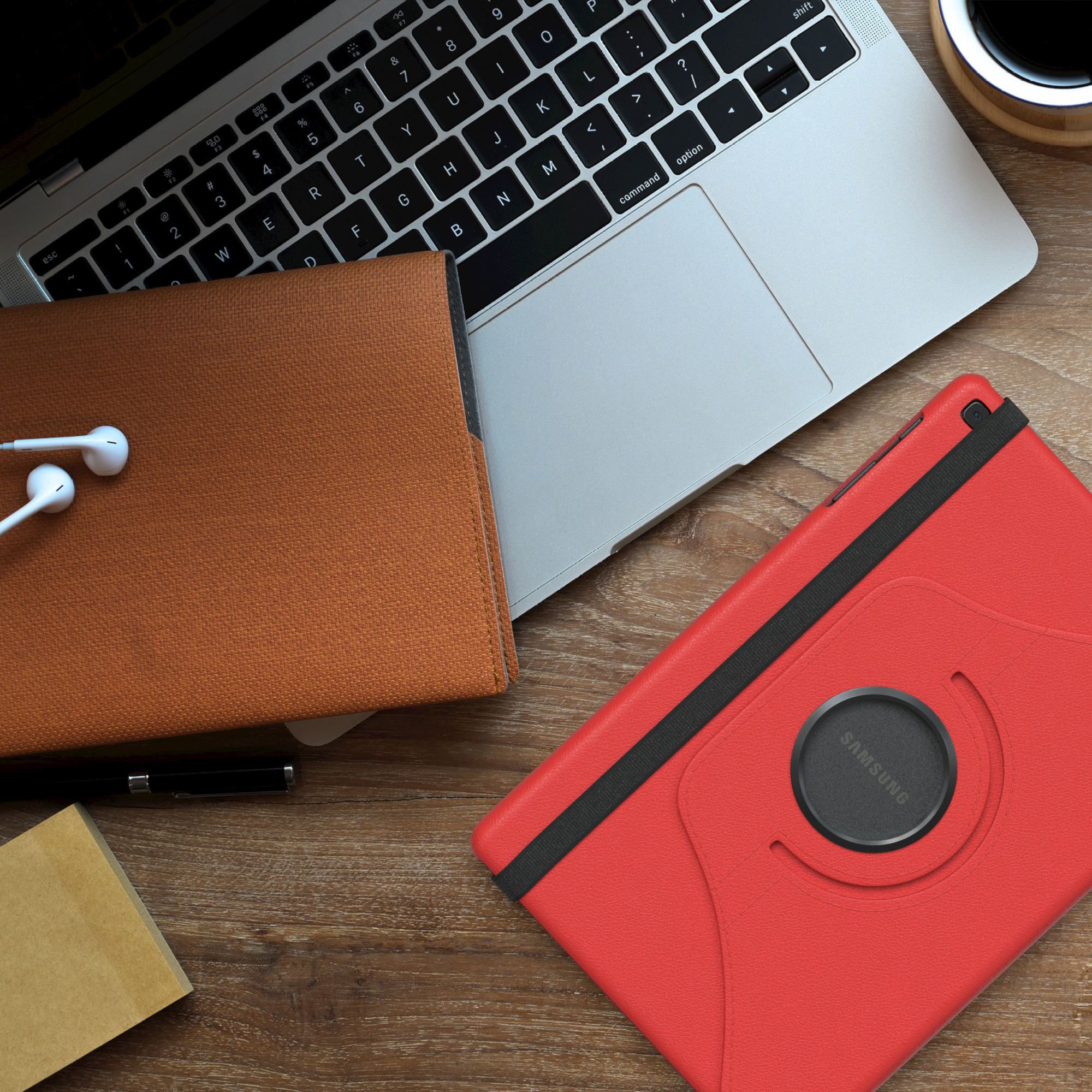 Ein Tablet mit roter Hülle und ein Laptop liegen auf einem Holzschreibtisch. Kopfhörer und ein Stift sind vorhanden.