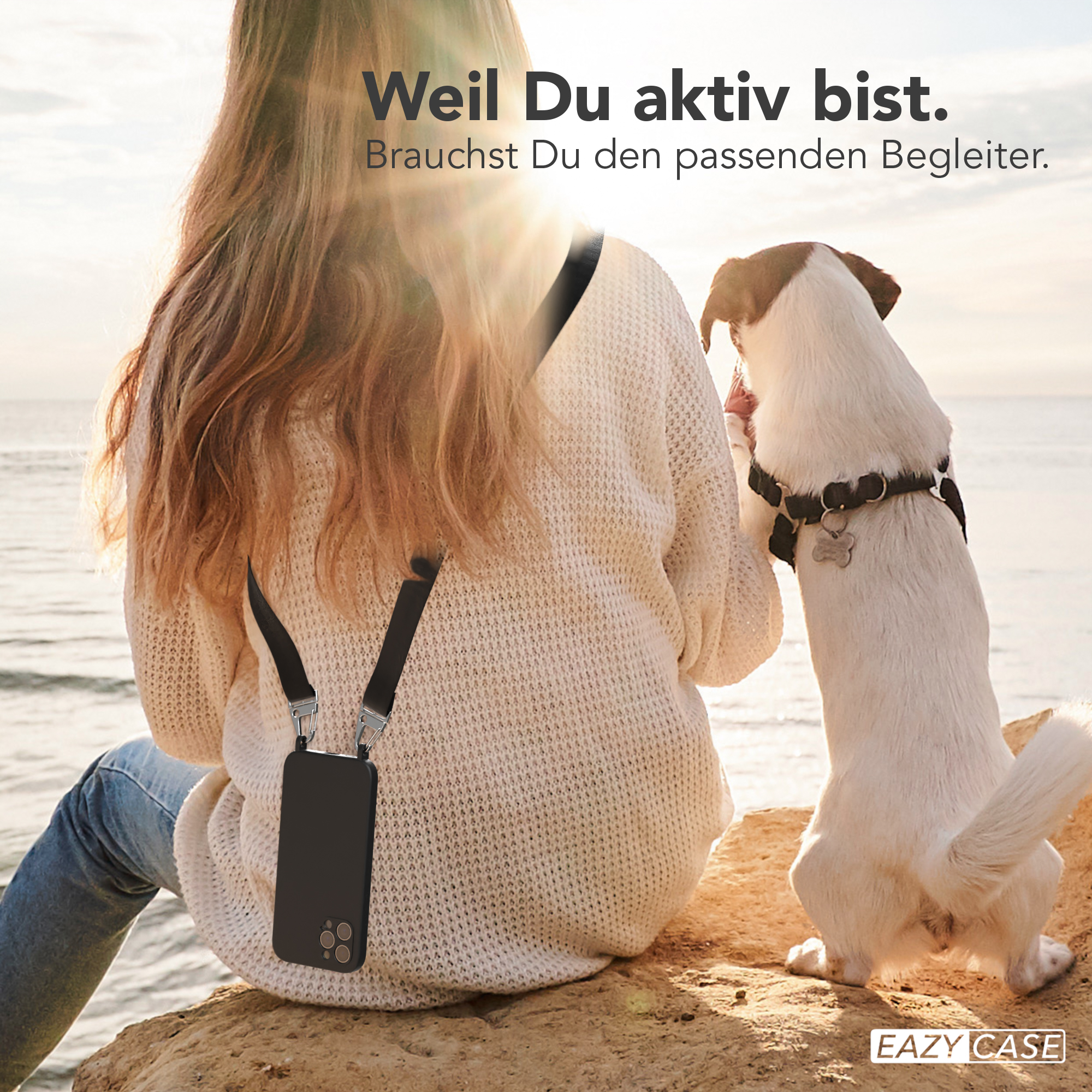 Frau mit Handyhülle, Hund neben ihr auf Felsen. Sonne scheint, heller Hintergrund.