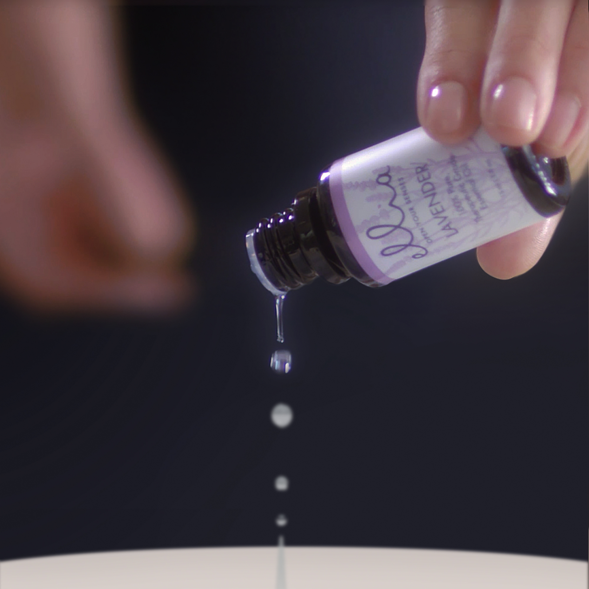 Mano che versa gocce di olio essenziale di lavanda. Gocce chiare cadono da una bottiglia nera.