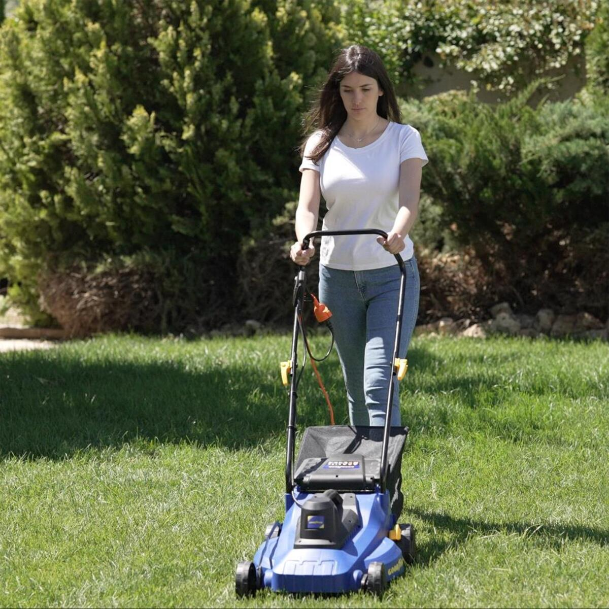 Mujer cortando un césped verde con un cortacésped azul. El césped está rodeado de árboles.