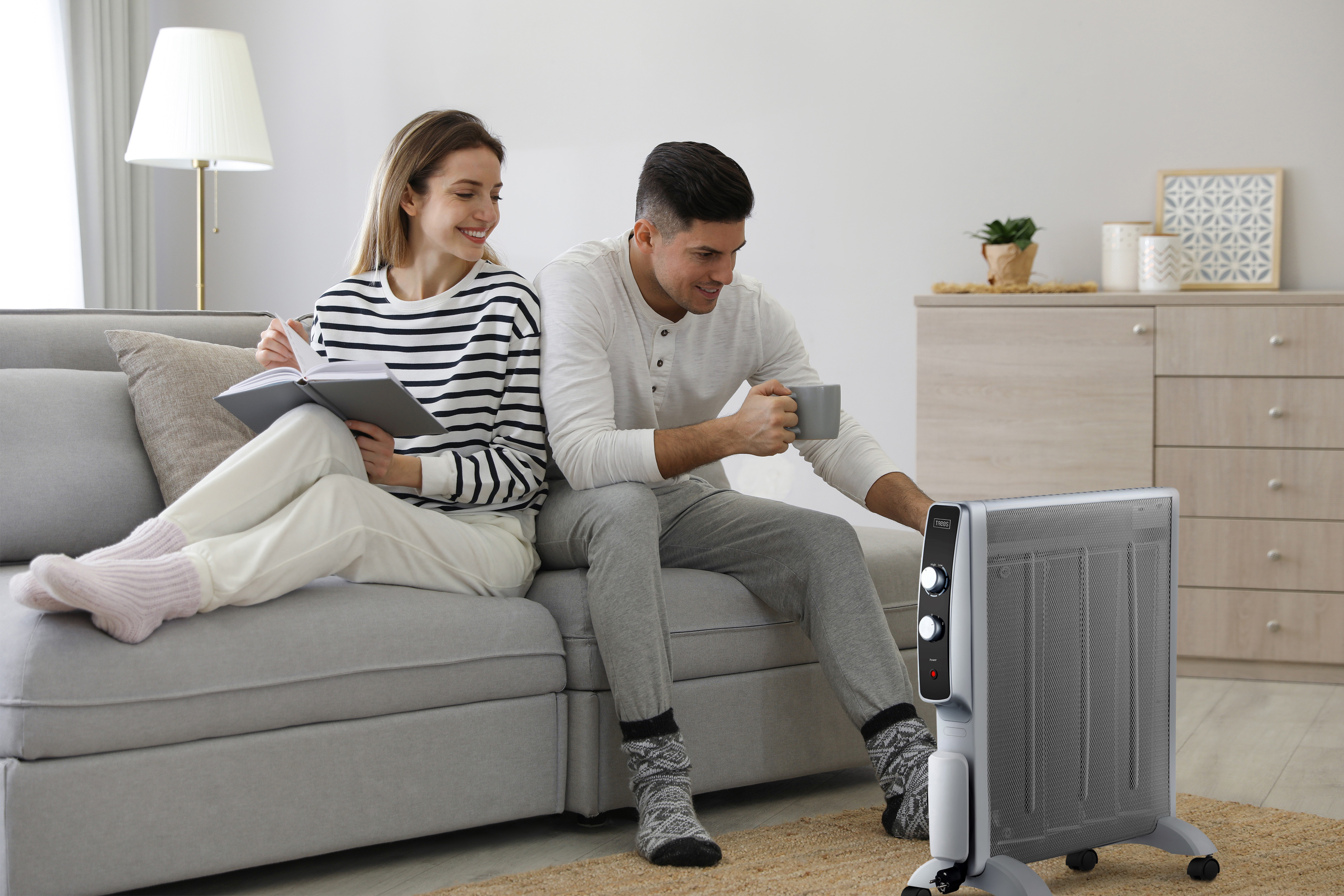 Paar sitzt auf einem Sofa, liest und benutzt eine Heizung. Wohnzimmer-Szene.