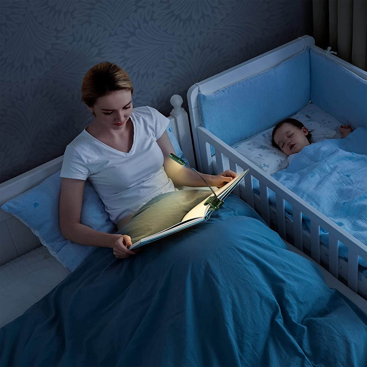 Frau liest Buch mit Clip-on-Licht, in der Nähe eines schlafenden Babys im Kinderbett.