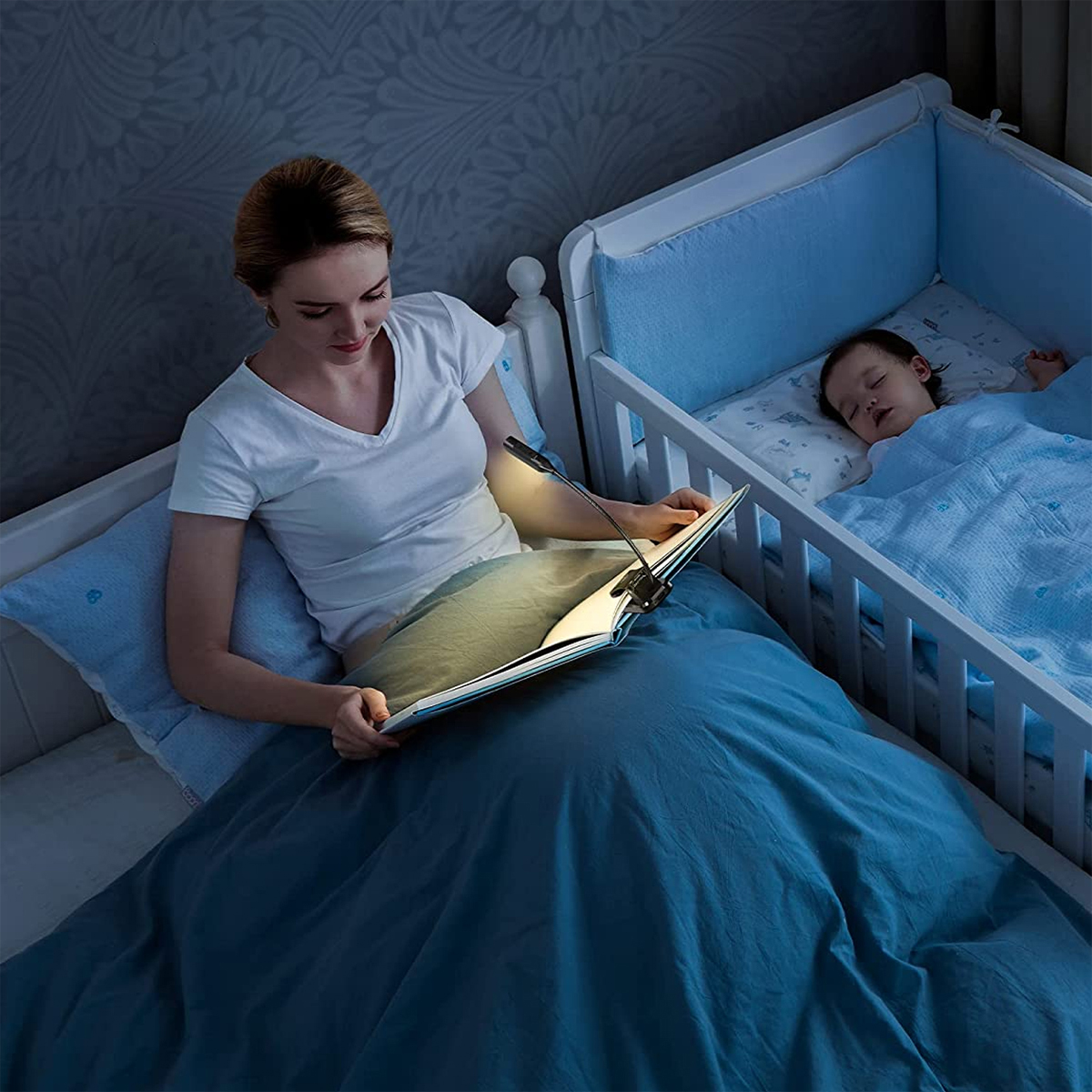Frau liest Buch mit Lampe im Schlafzimmer. Ein Baby schläft im Kinderbett.