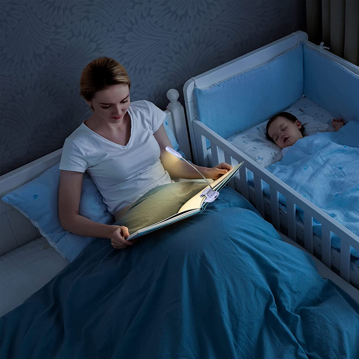 Frau liest am Babybett. Buch wird von flexiblem Licht beleuchtet. Baby schläft. Nachtszene.