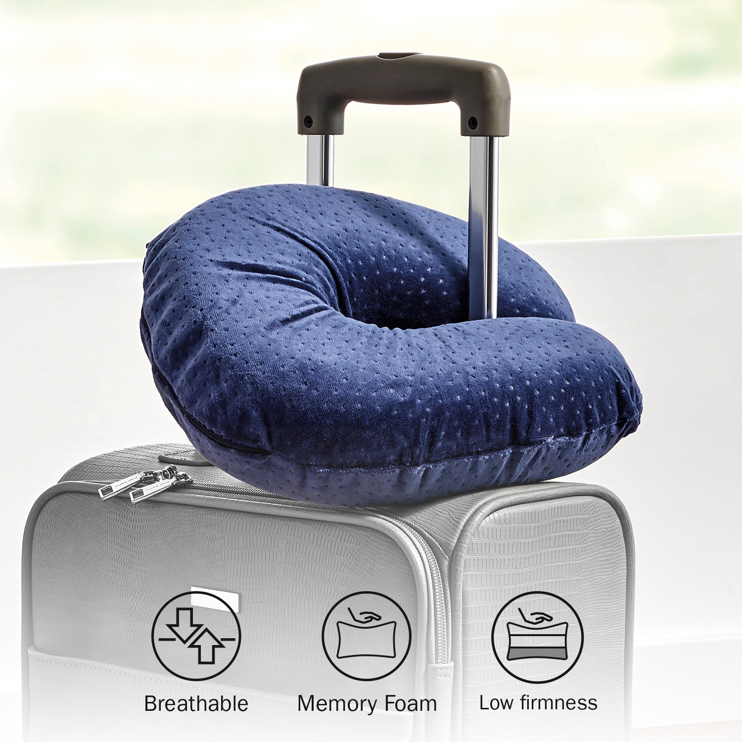 Una almohada de viaje azul encima de una maleta gris.