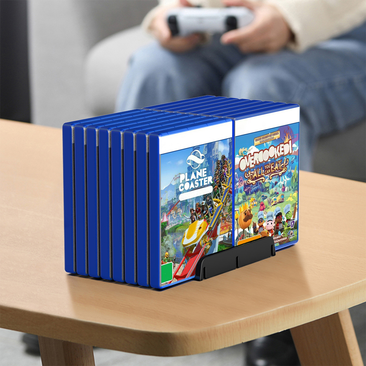 Spiele auf einem Tisch. Blaue Spielkassettenhalter, mit zwei sichtbaren Spielcovern. Person hält Controller.