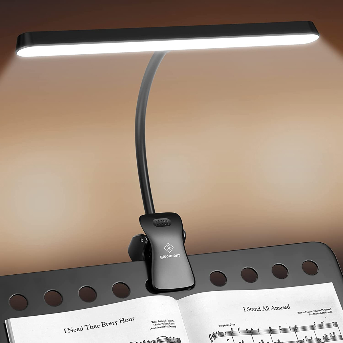 Lámpara de escritorio negra con cuello flexible. Está sujeta a un atril con partituras.