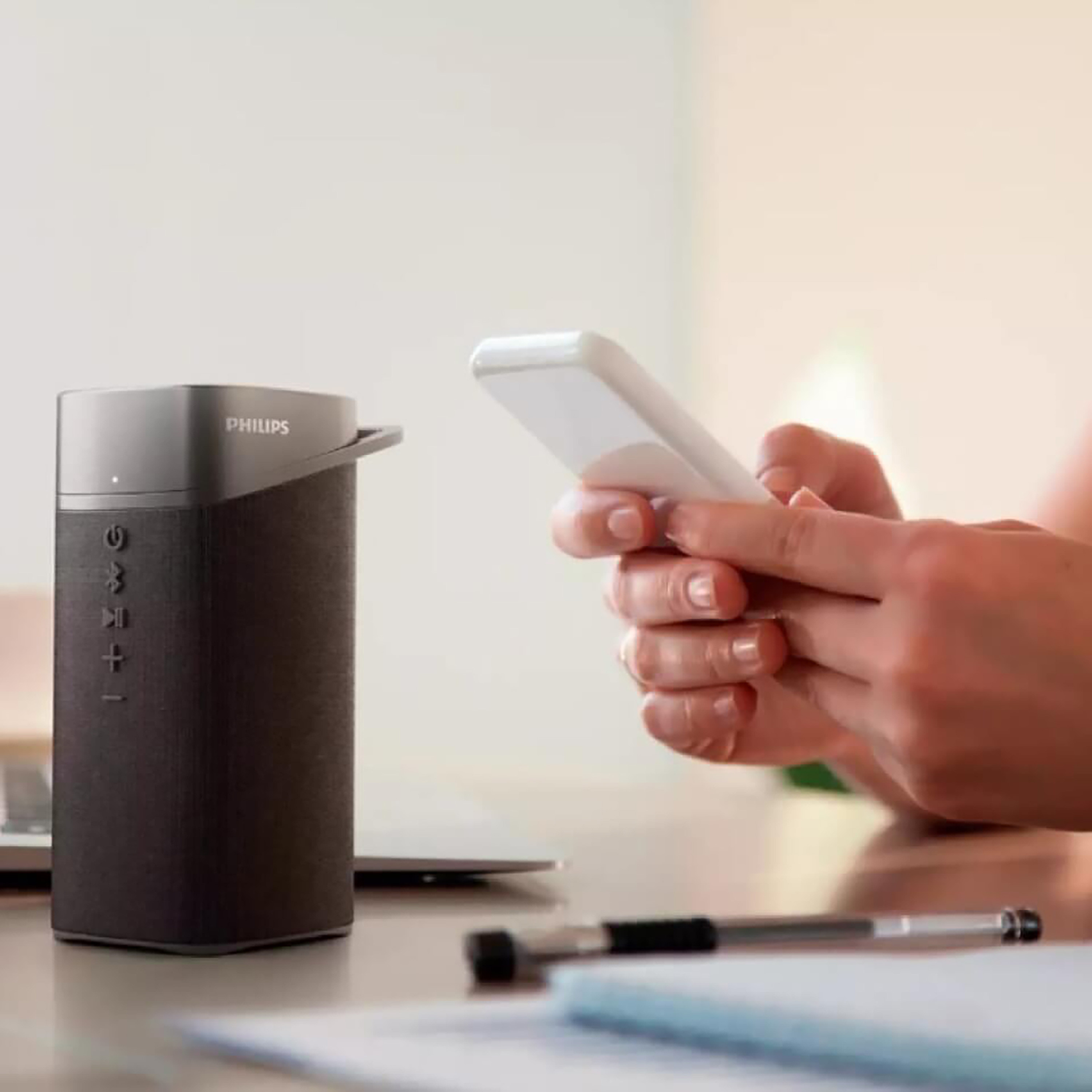 Un altoparlante Philips nero e argento, con una persona che tiene un telefono sullo sfondo.