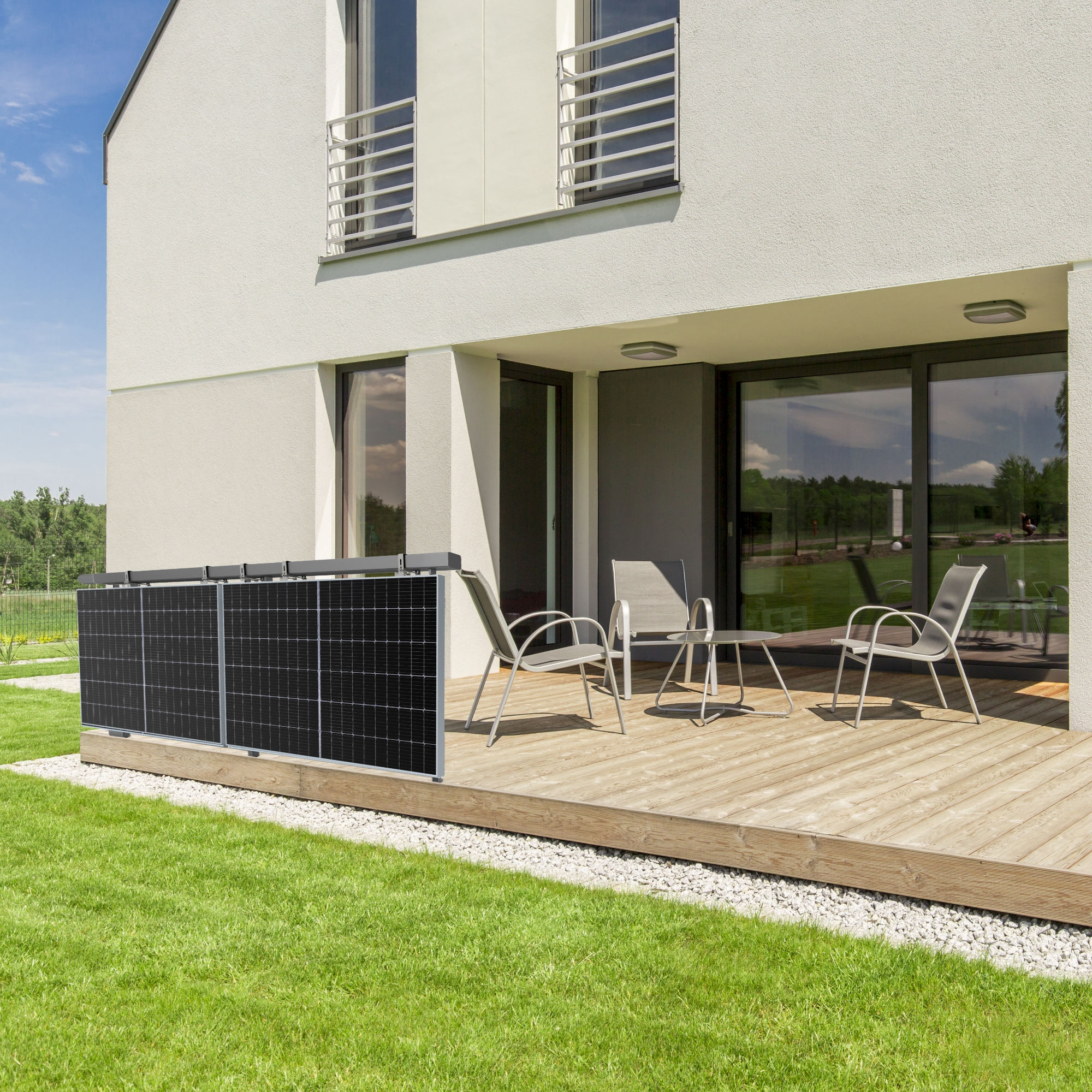 Modernes Haus mit Solarpanelen auf Holzterrasse, mit Stühlen und Tisch, unter blauem Himmel.