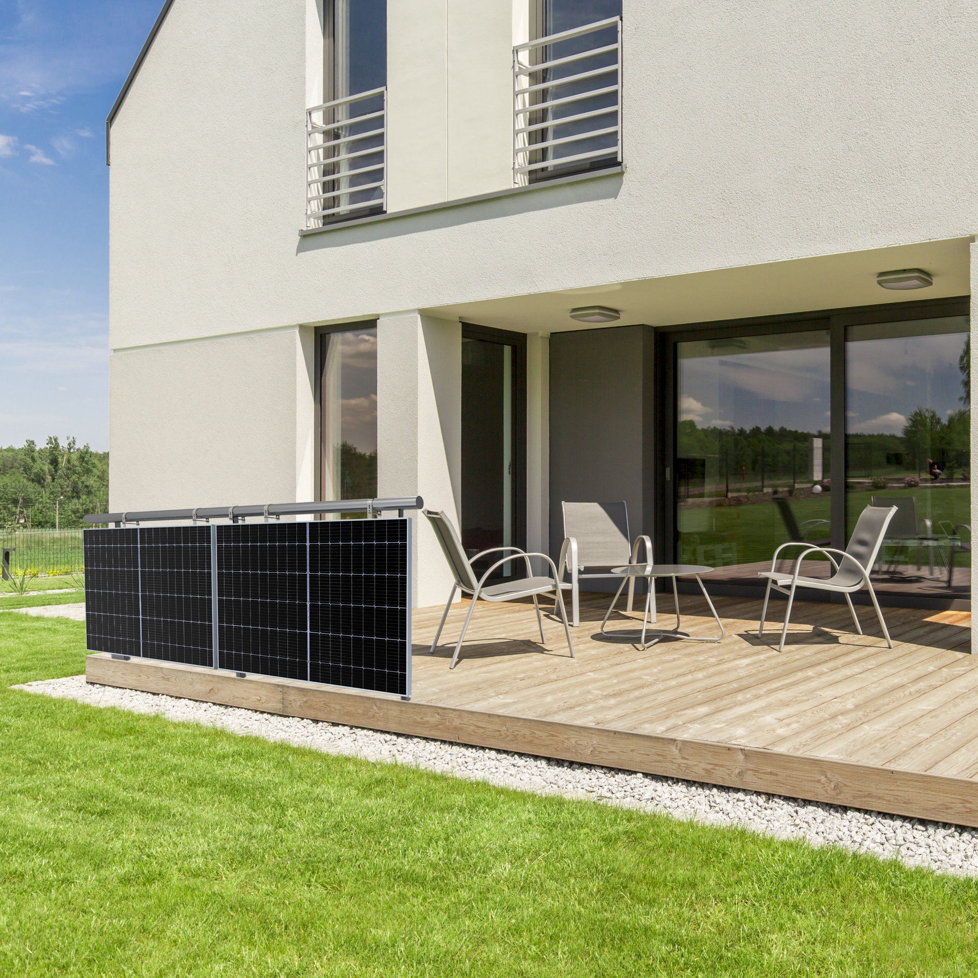 Modernes Haus mit Holzterrasse und Rasen. Solarzaun und Gartenmöbel sind vorhanden.