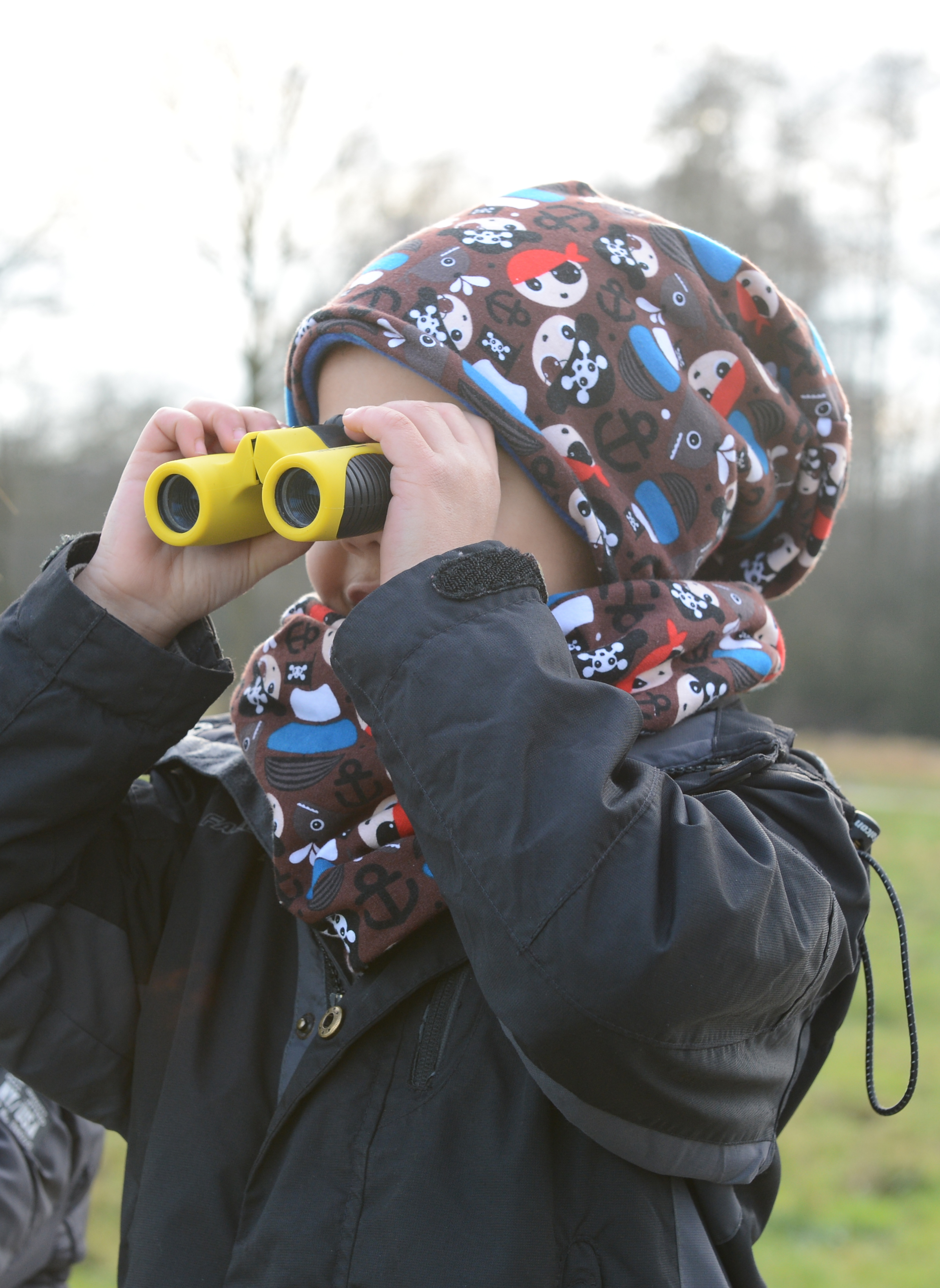 Dziecko z lornetką na coś patrzy.