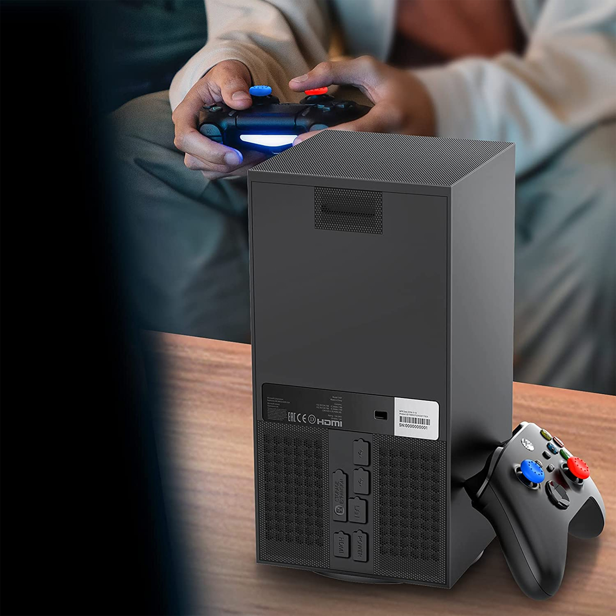 Eine schwarze Spielkonsole mit zwei Controllern, einer in Gebrauch. Eine Person hält einen Controller.