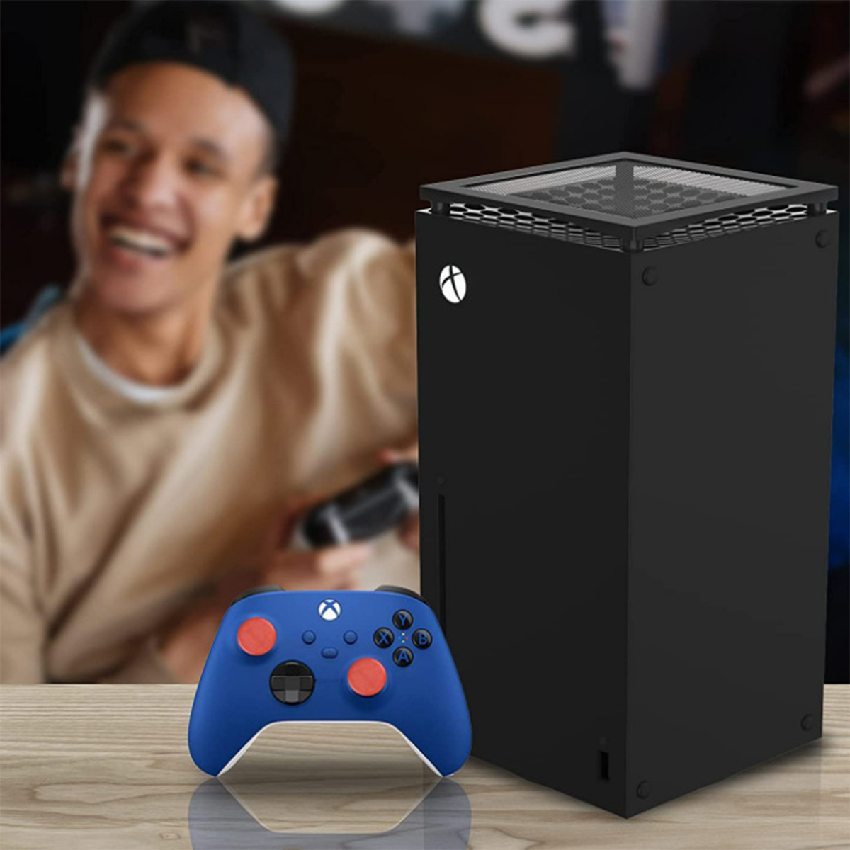 Xbox Series X Konsole, Controller und Person im Hintergrund, alles auf einer Holzoberfläche.