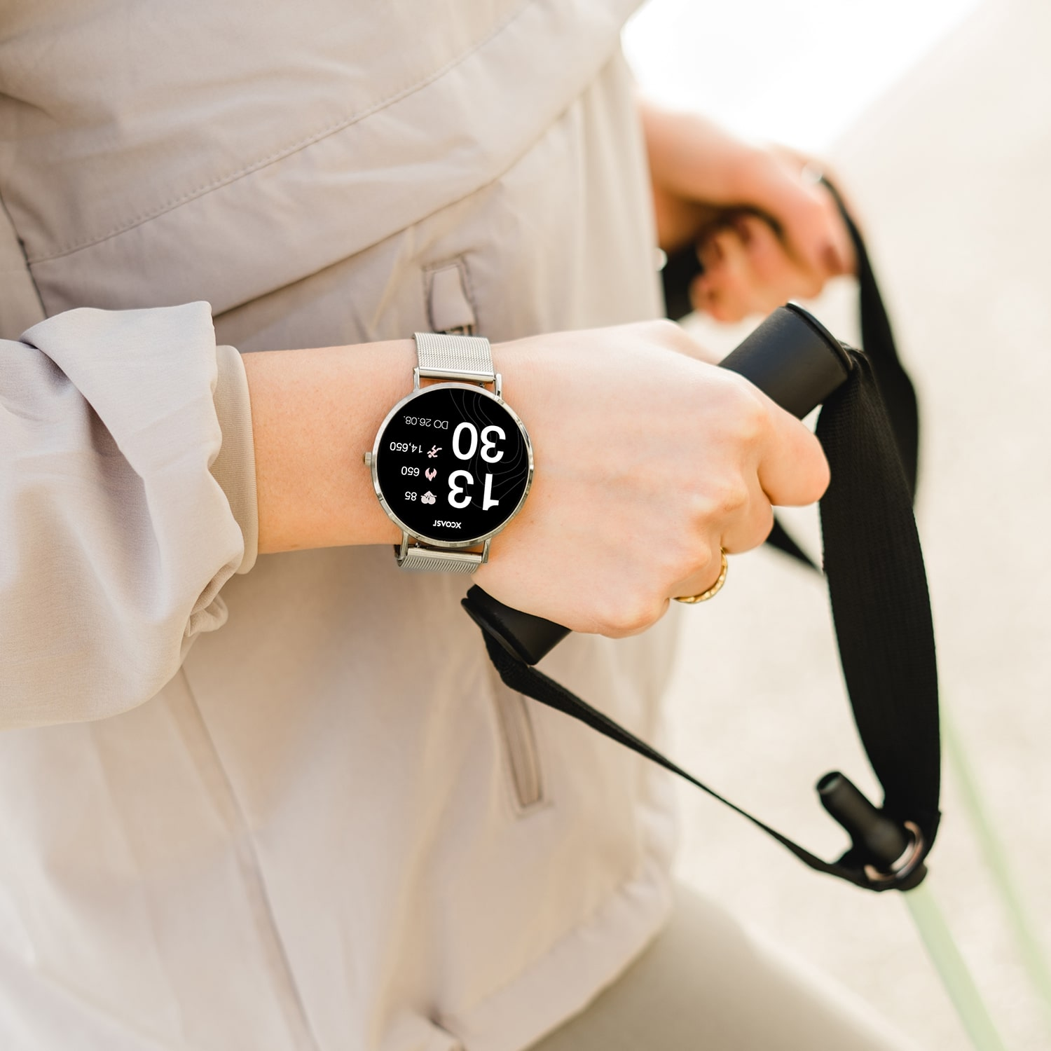 Eine Person, die eine Smartwatch mit silbernem Armband trägt und Trainingsgeräte hält.