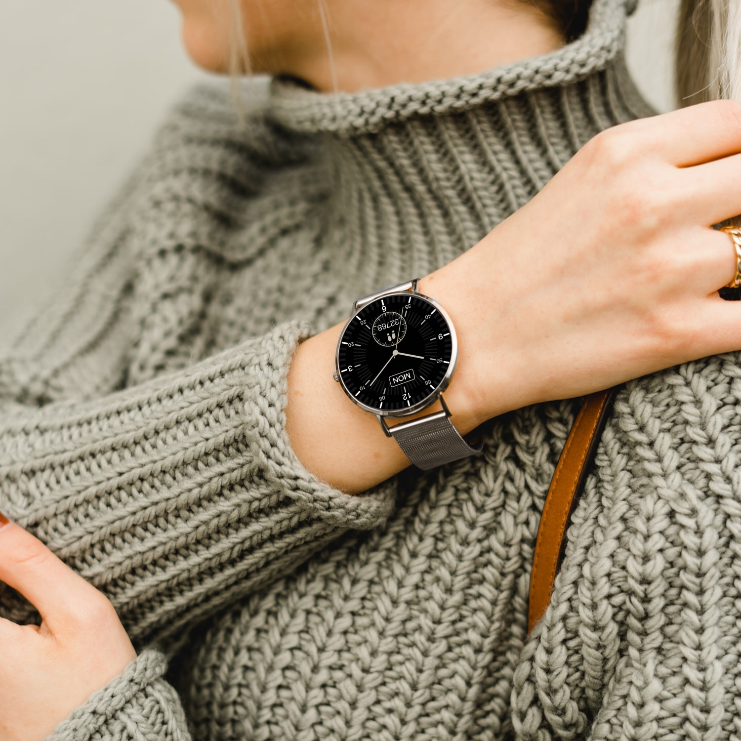 Frau mit grauem Pullover, Uhr am Handgelenk. Das Zifferblatt ist schwarz mit silbernem Band.