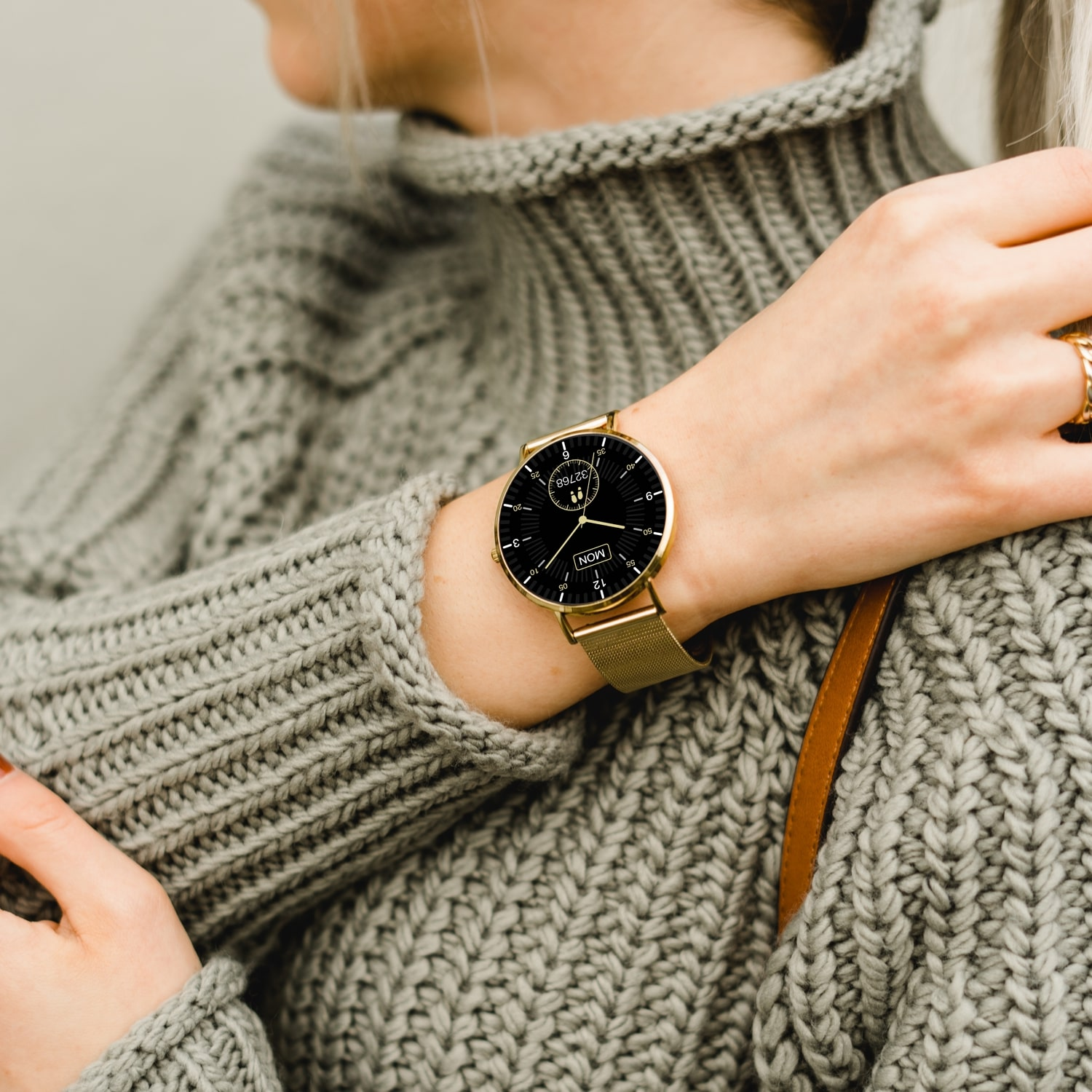 Frau trägt goldene Uhr, goldenes Armband, am Handgelenk, grauer Pullover, Nahaufnahme.
