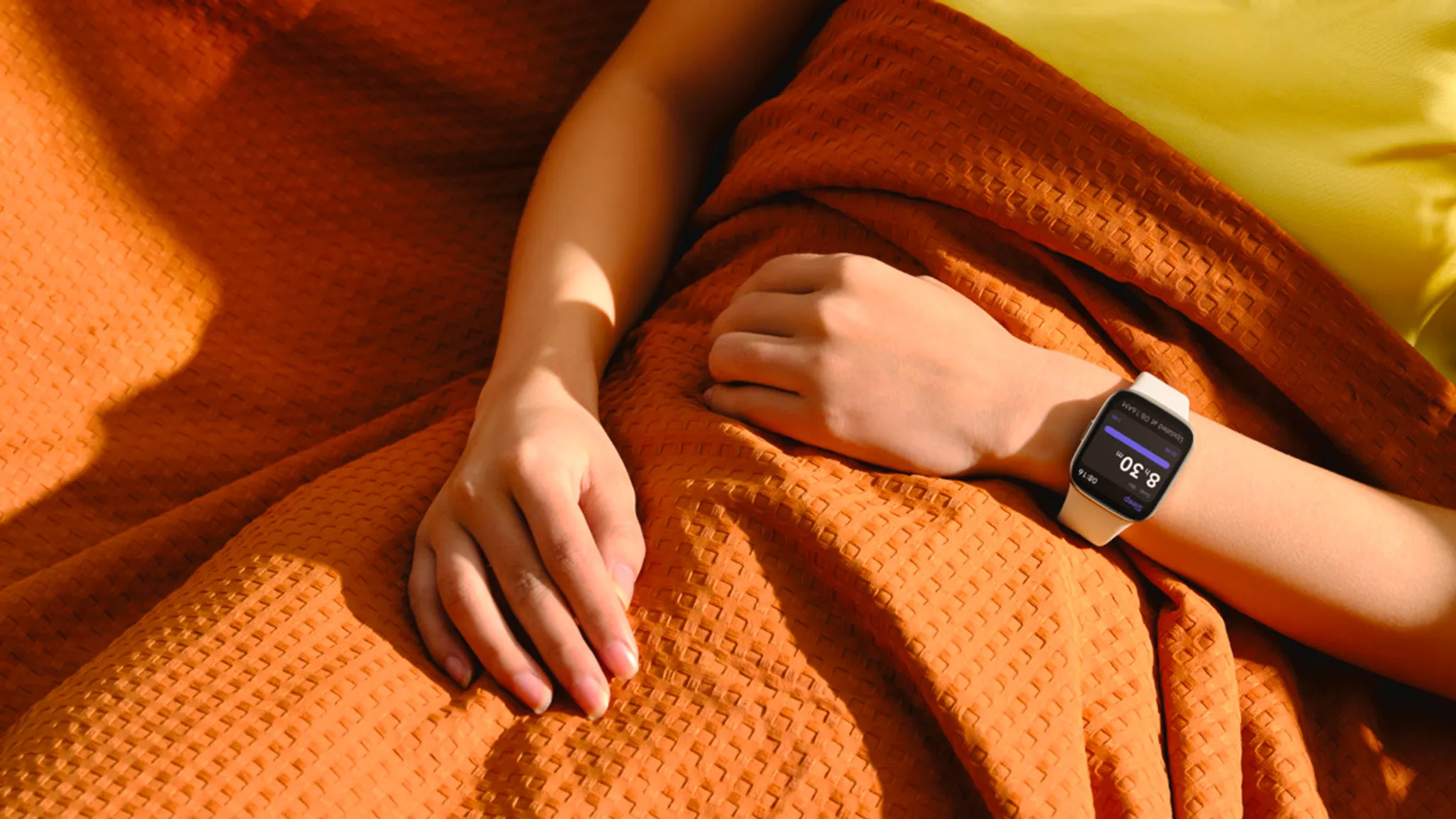 Braccio di donna con uno smartwatch bianco su una coperta arancione. L'orologio mostra le 8:30.