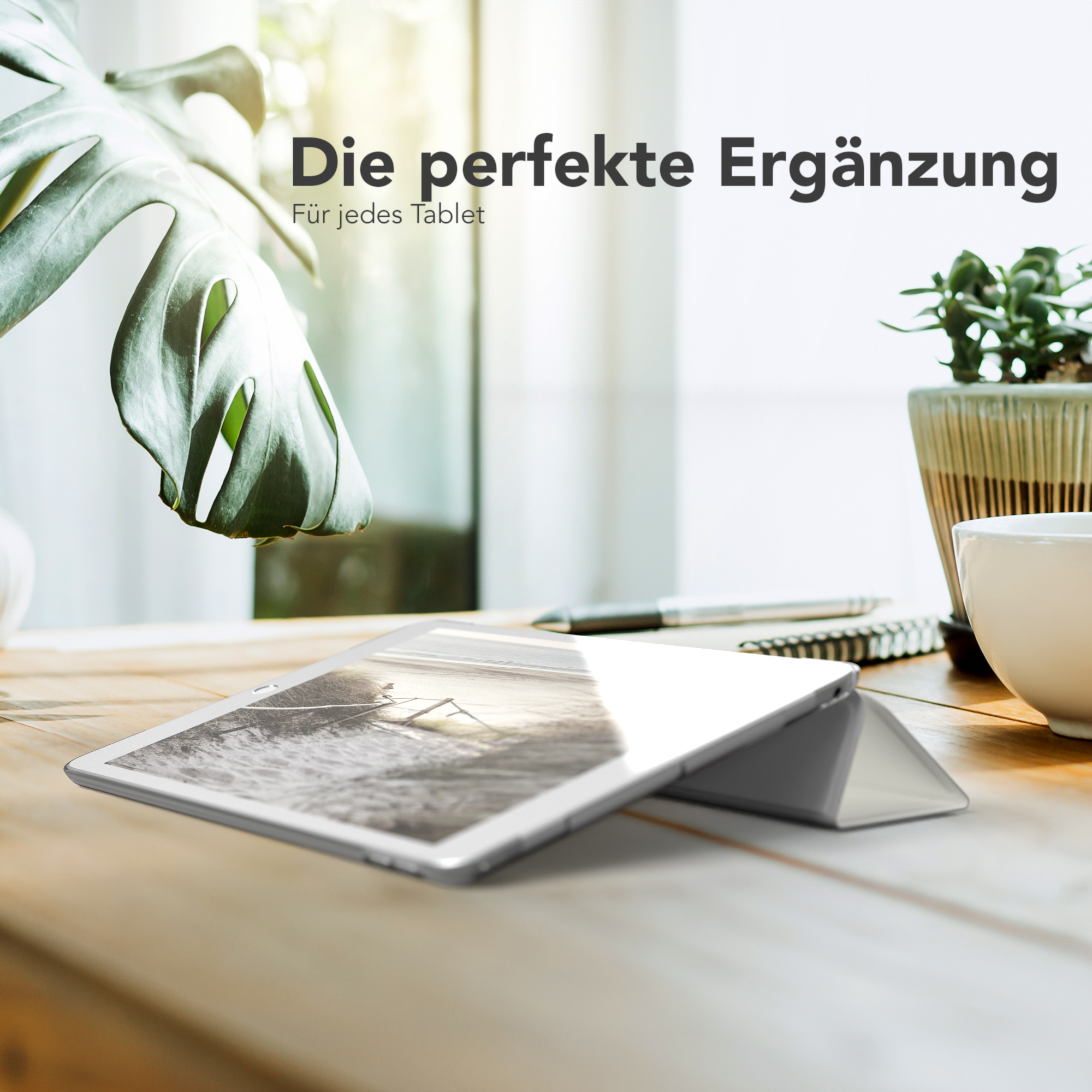 Ein Tablet, das von einer Hülle auf einem Holztisch aufgestellt wird, mit Topfpflanze und Kaffeetasse.