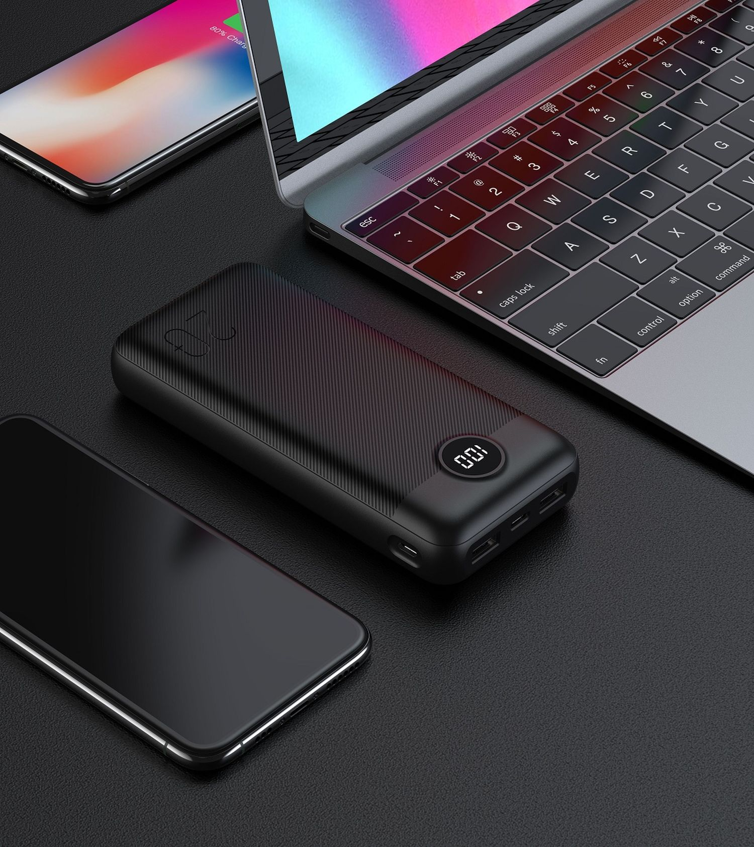 Power bank nero con display, smartphone e laptop su una superficie nera.