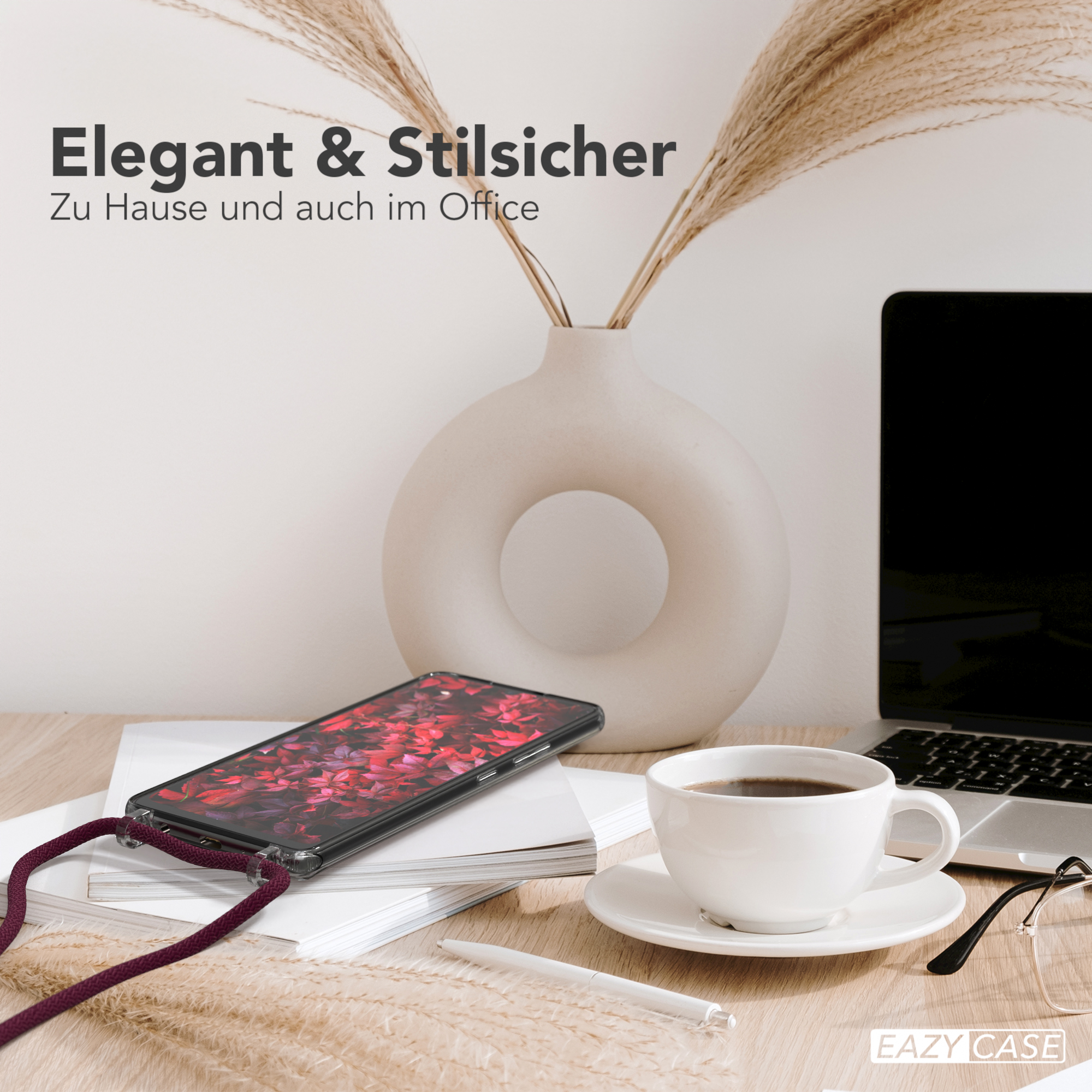 Telefon mit bordeauxfarbenem Band auf Schreibtisch mit Kaffee und Pampasgras-Vase.