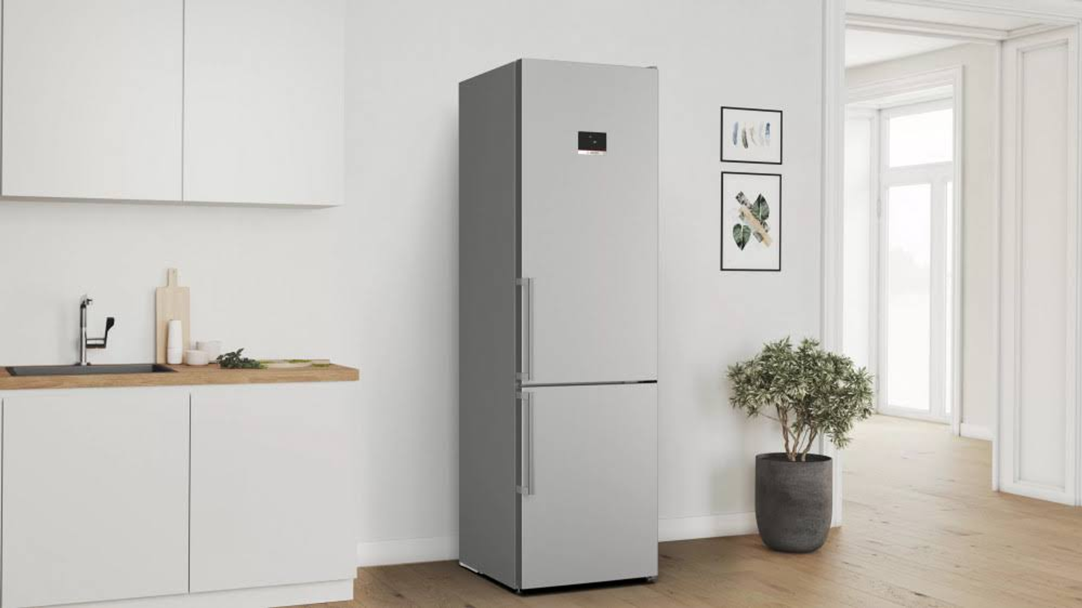 Refrigerador plateado con un fondo de cocina blanco, con una planta y cuadros.