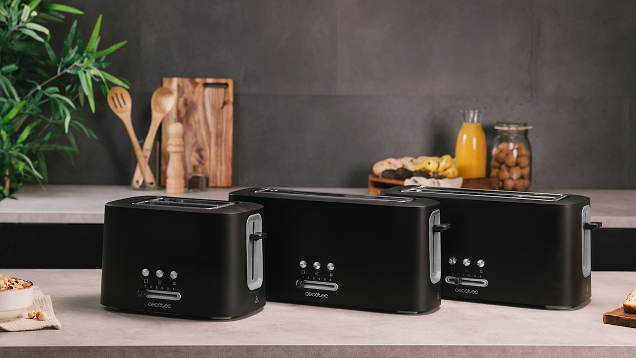 Three black toasters on a grey surface. There is a wooden cutting board and some jars on the back.