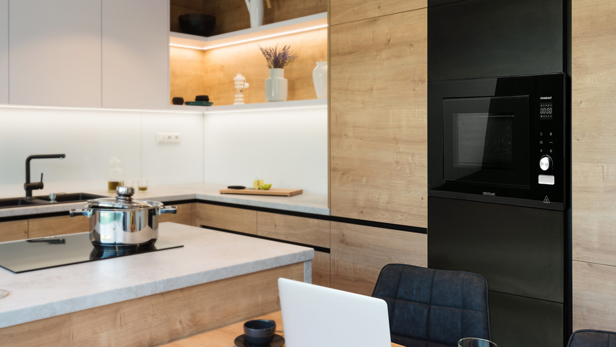 Nowoczesna kuchnia z drewnianymi szafkami, garnkiem ze stali nierdzewnej na płycie grzejnej i wbudowaną kuchenką mikrofalową.