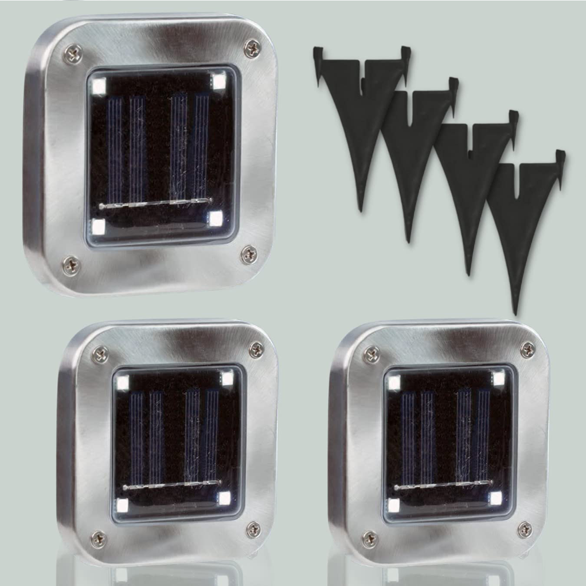 Quatre lampes solaires argentées et piquets noirs, sur fond vert clair.