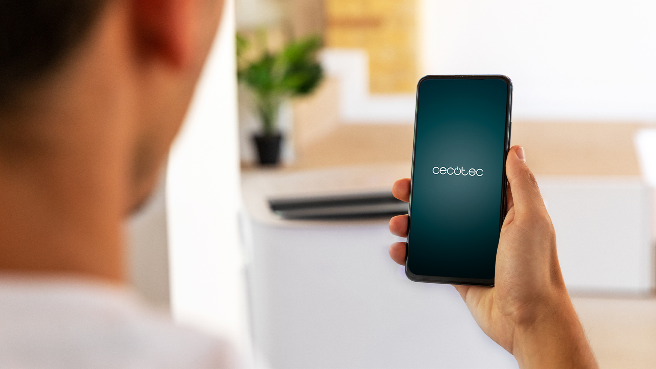 Osoba trzymająca telefon z logo Cecotec na ekranie. Rozmyte tło.