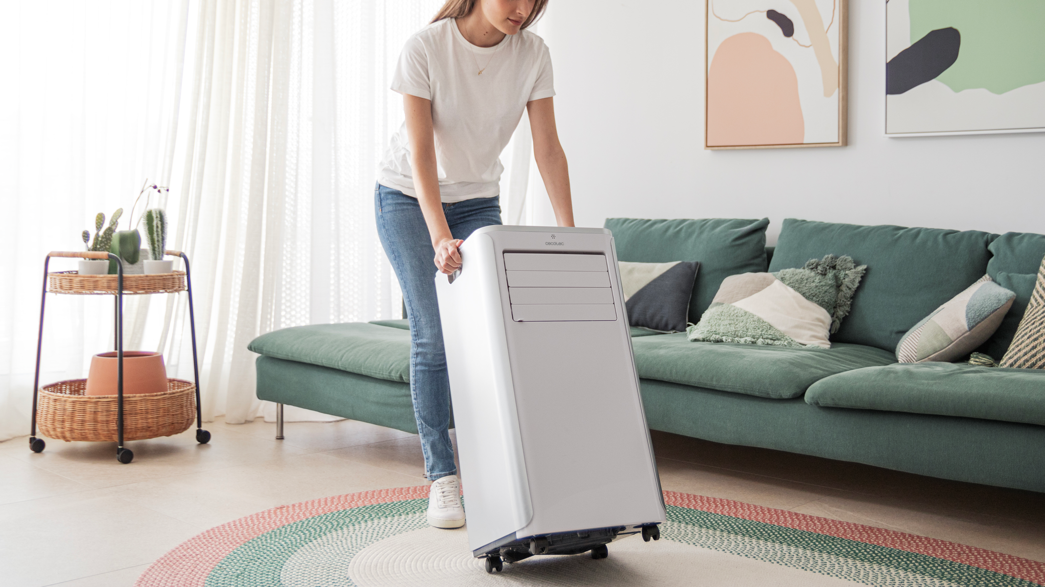 Kobieta tocząca białą przenośną klimatyzację na kółkach w salonie.