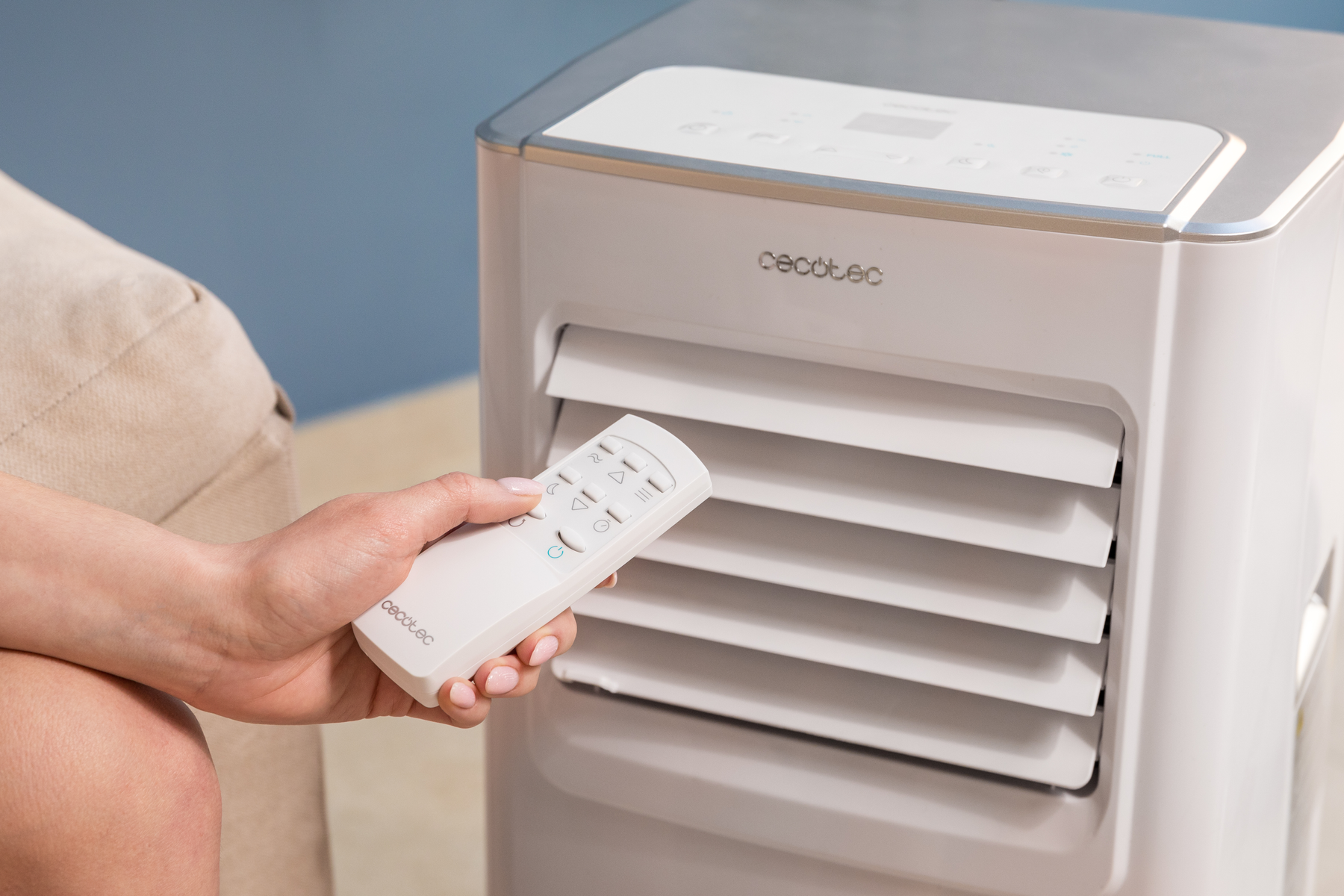 Kobieta trzymająca pilota obok białej i szarej chłodziarki powietrza.