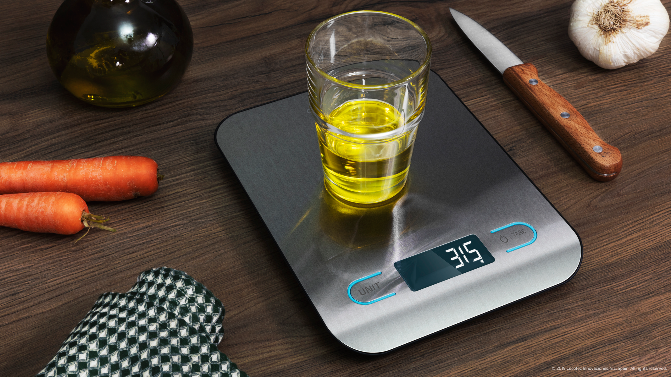 Bilancia da cucina digitale con bicchiere d'olio, carote, coltello e panno.