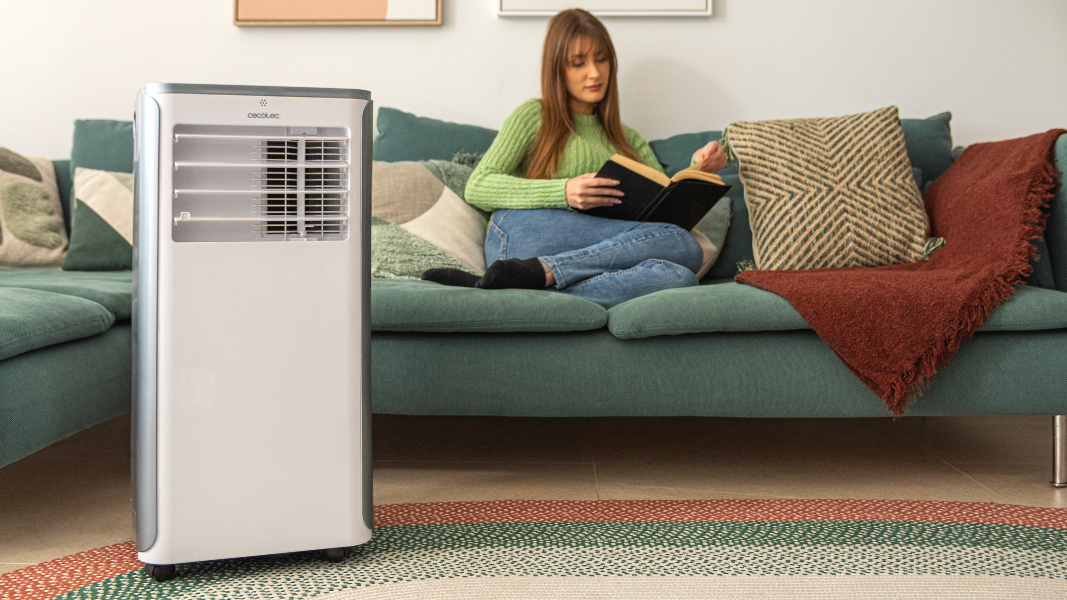 Kobieta czyta na kanapie, obok klimatyzator. Zielony, biały i szary. Pokój ma dywan.