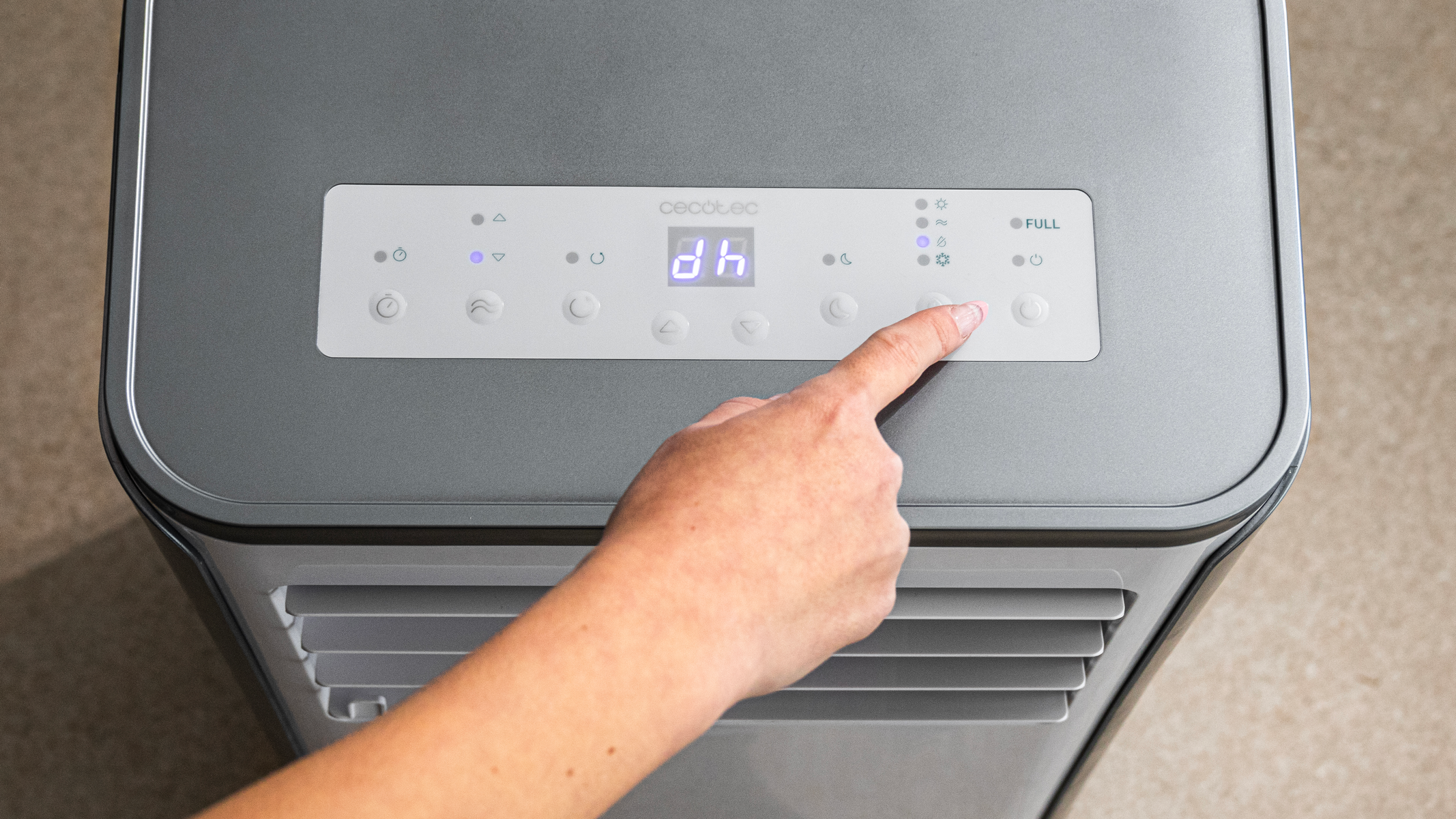 Dłoń naciskająca przycisk na szarej chłodziarce powietrza.