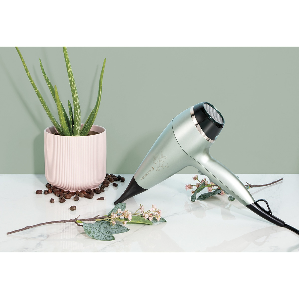 Minzgrüner Haartrockner mit schwarzen Akzenten auf weißer Oberfläche mit Aloe Vera und Blumen.
