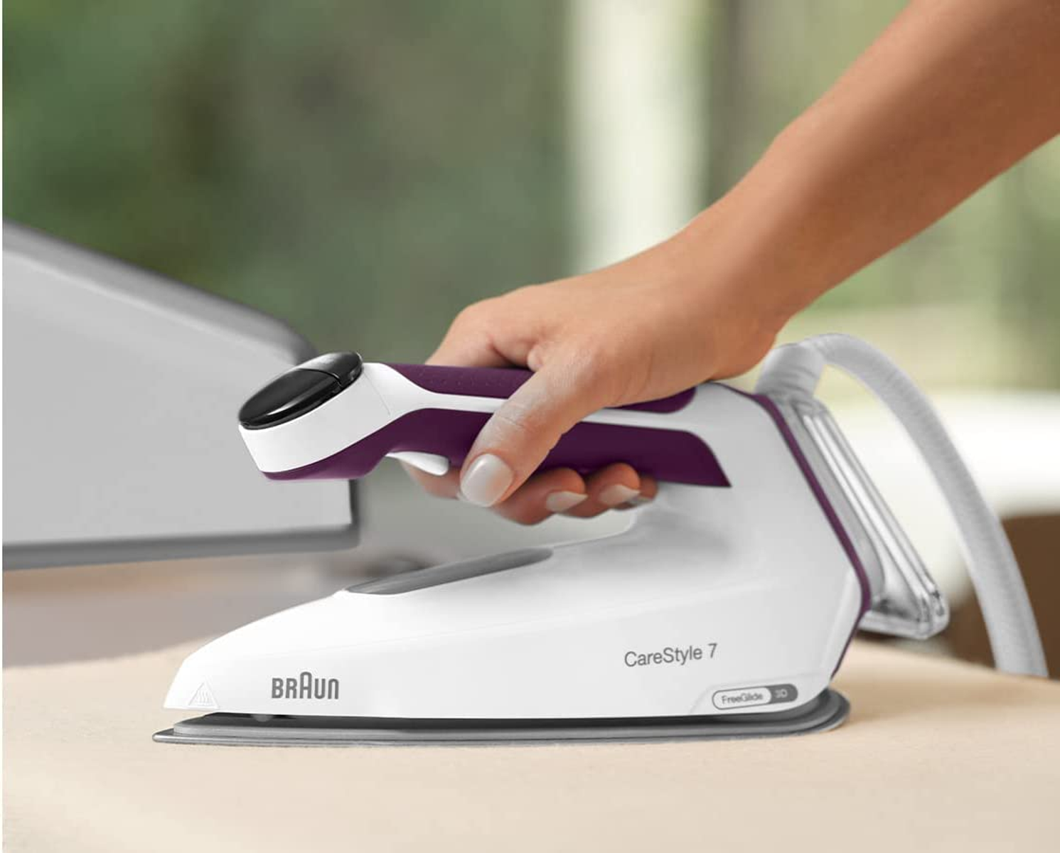 Ein weißes und lila Bügeleisen mit einer Hand, die Stoff bügelt. Der Text 'Braun CareStyle 7' ist sichtbar.
