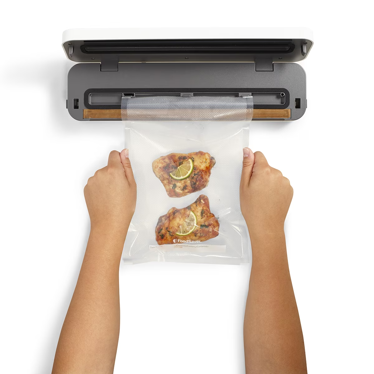 Dłonie trzymają przezroczystą plastikową torbę z jedzeniem w środku, umieszczoną w zgrzewarce.