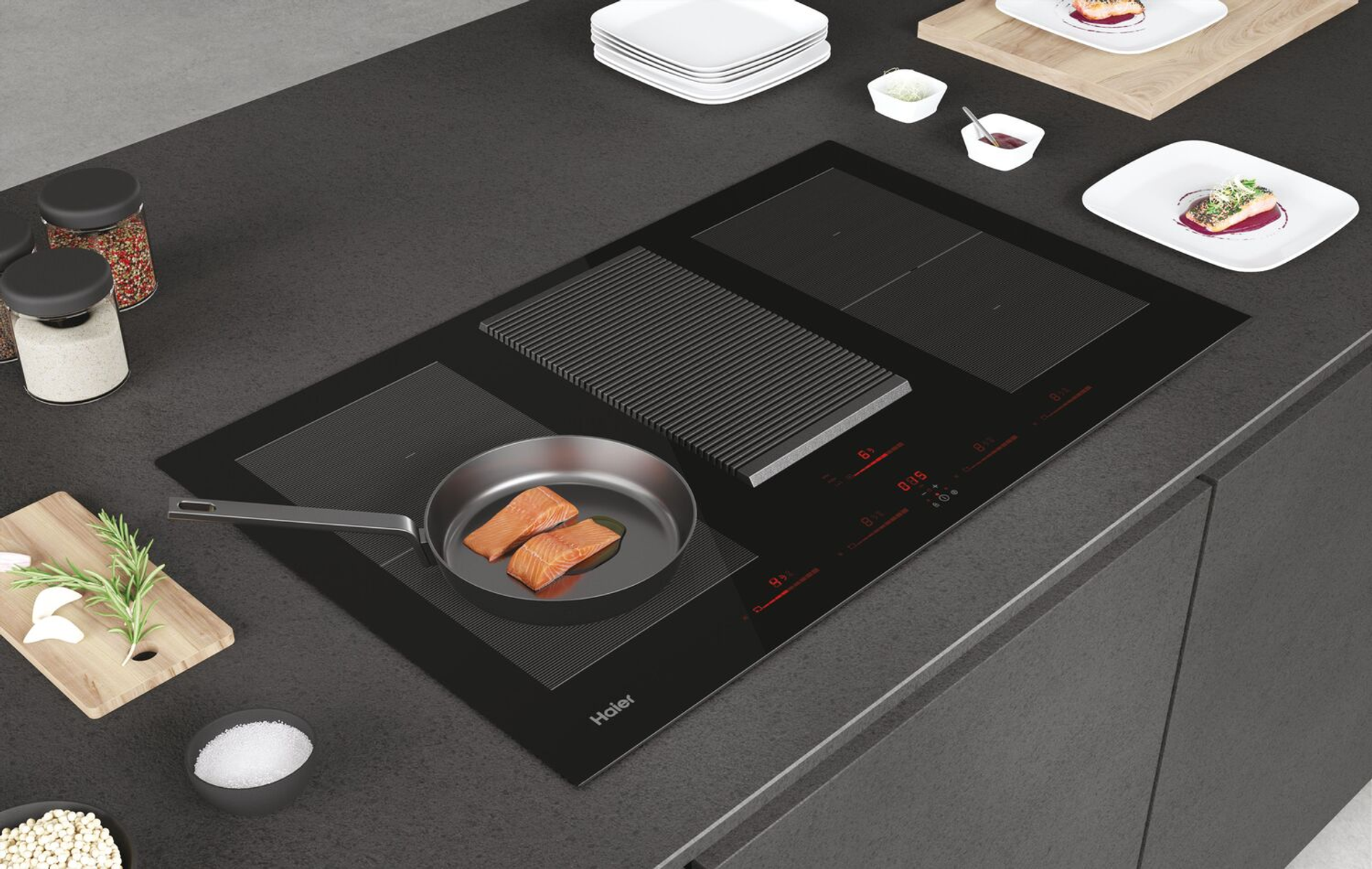 Una placa de inducción negra con una sartén con salmón. Otros platos e ingredientes son visibles.