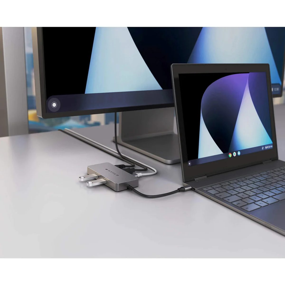 Portátil y monitor conectados a un concentrador. El concentrador tiene puertos USB. Escritorio blanco.