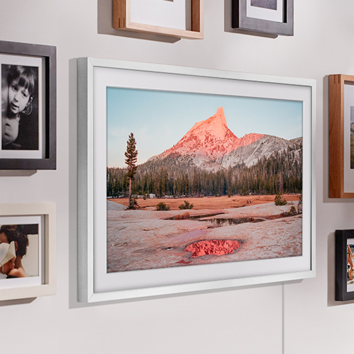 Oprawione zdjęcie górskiej scenerii wisi na ścianie z innymi zdjęciami.