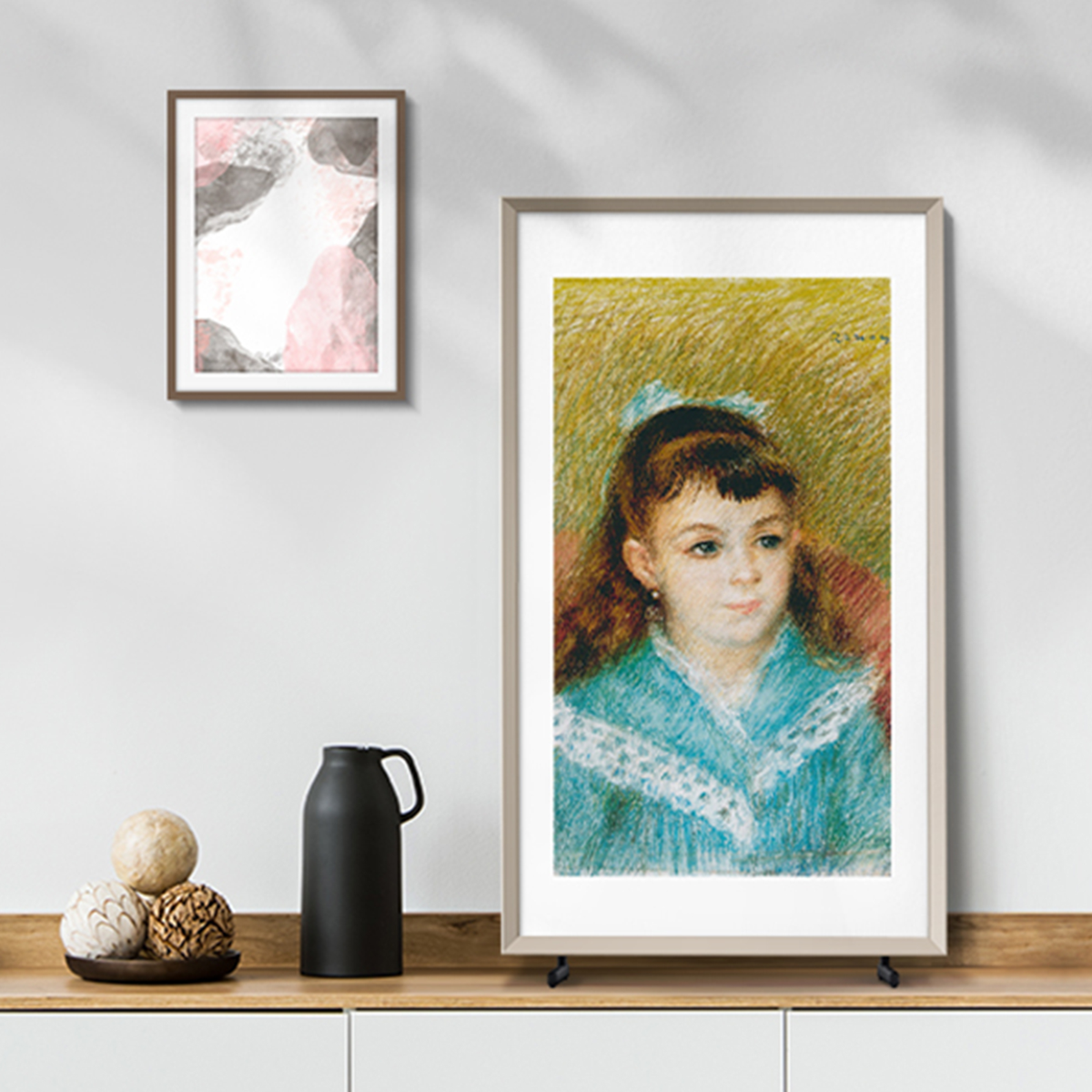 Dwa oprawione dzieła sztuki na drewnianej półce. Jeden to portret dziewczyny w niebieskim.