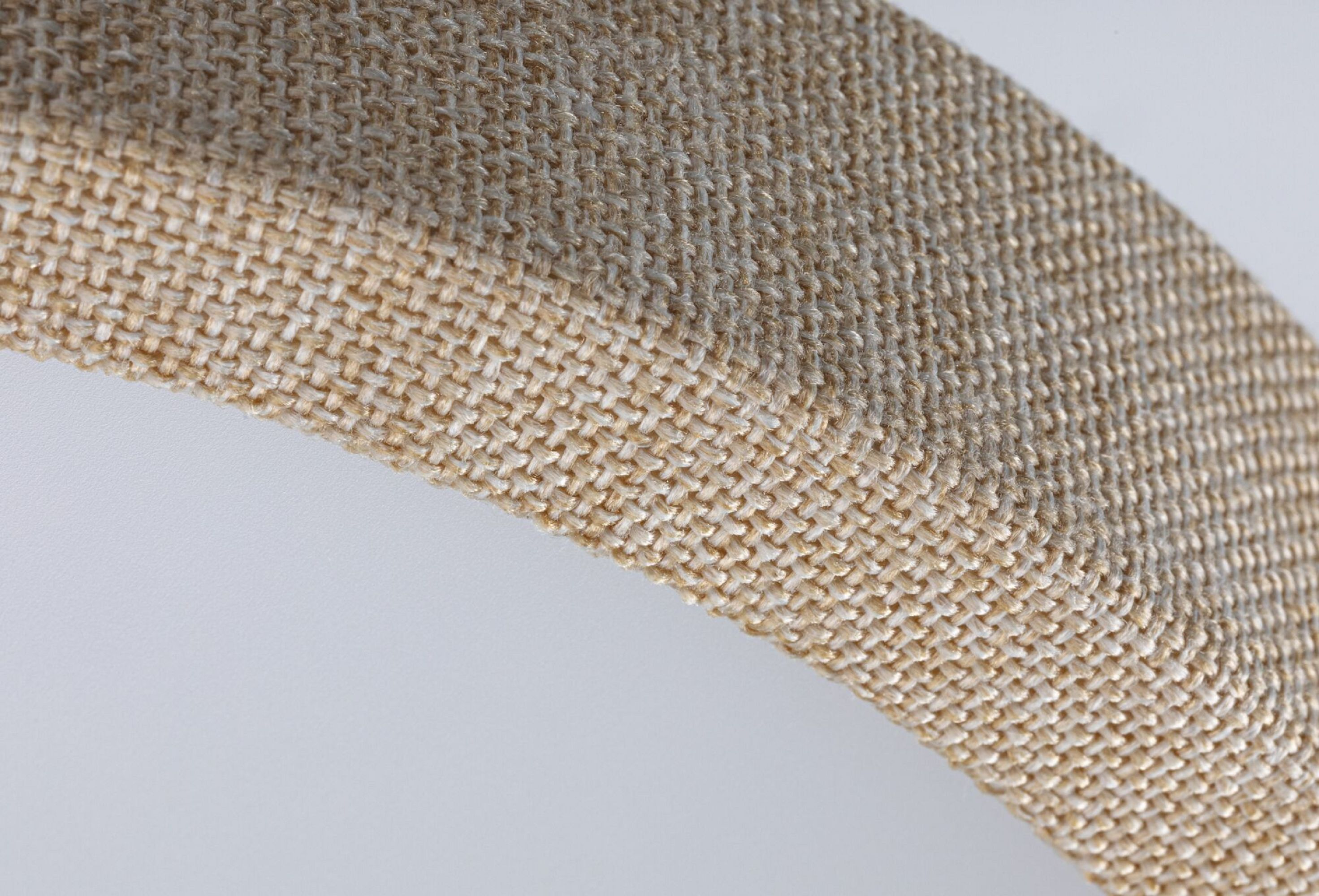 Zbliżenie tkanego materiału o zakrzywionym kształcie. Tekstura jest beżowa, z białym tłem.