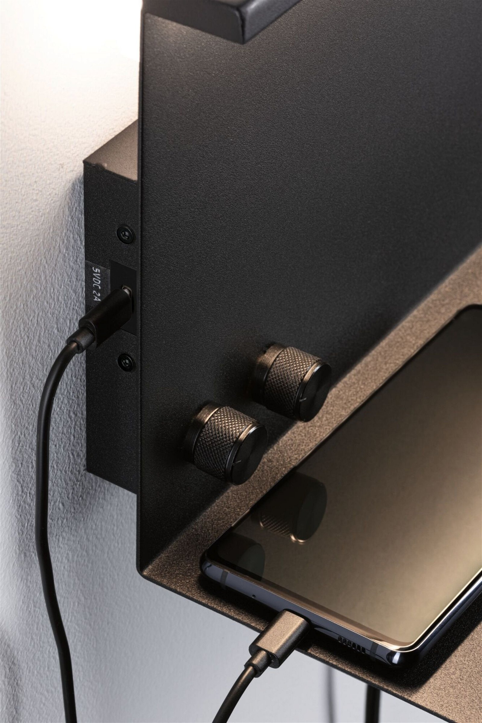 Czarna półka naścienna ze stacją ładowania i przechowywania telefonu.