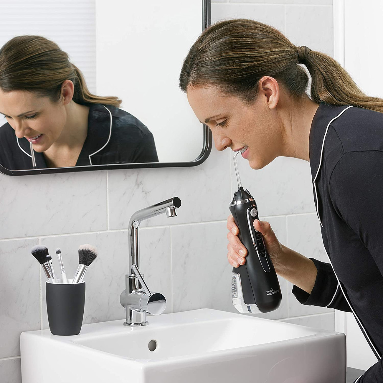 Femme utilisant un hydropulseur dans la salle de bain. Le miroir reflète son visage.